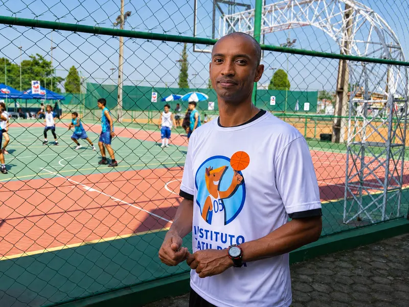 Representante do Instituto Tatu Bola em frente à quadra, com crianças jogando ao fundo